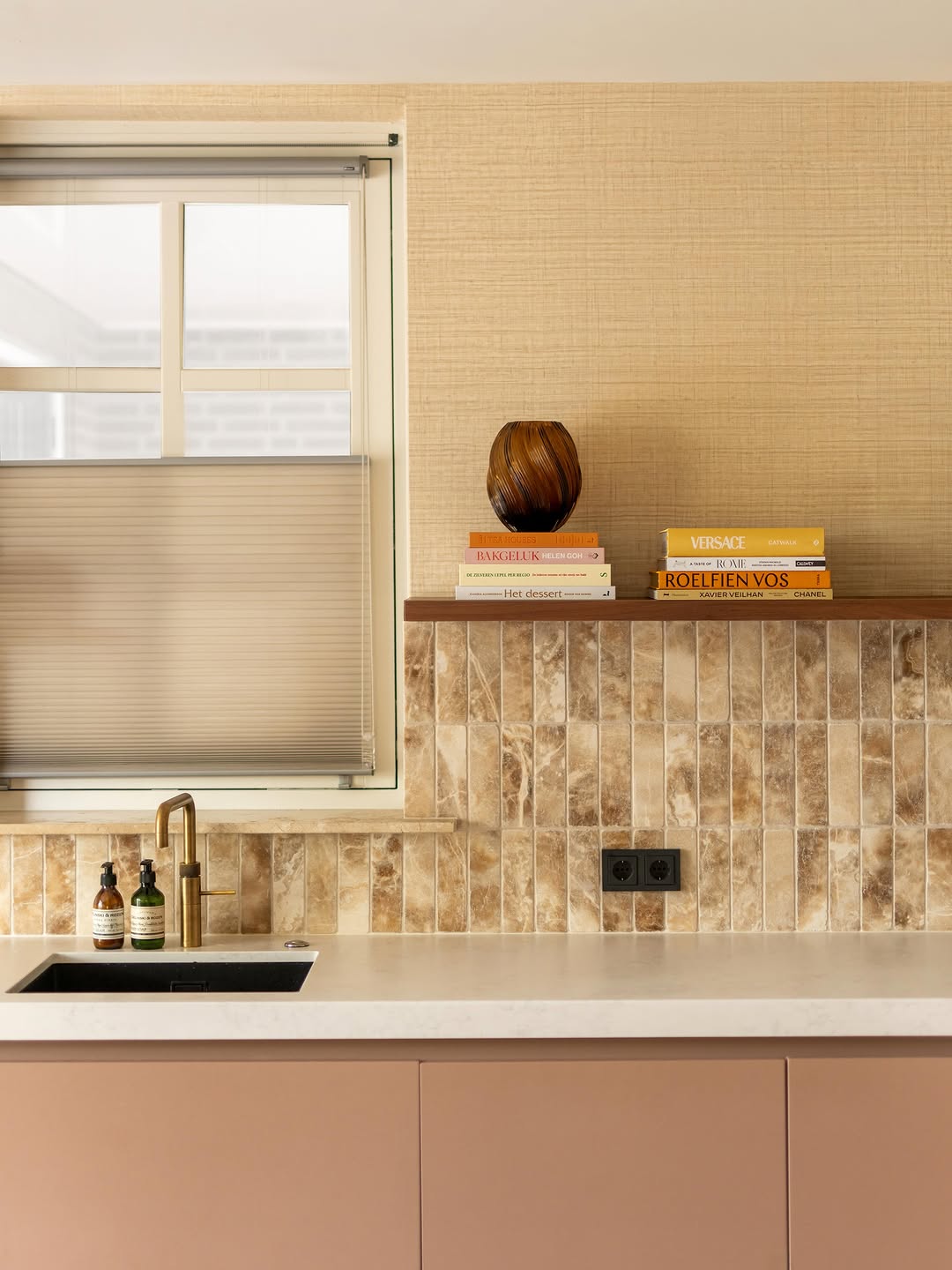 Keuken met verticaal geplaatste Brick Crema Onyx tegels, een licht werkblad, goudkleurige kraan en zachte kastkleuren.