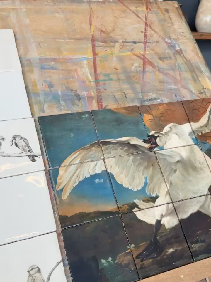 Tegeltableau met een witte zwaan met uitgespreide vleugels, naast witte tegels met vogeltekeningen.