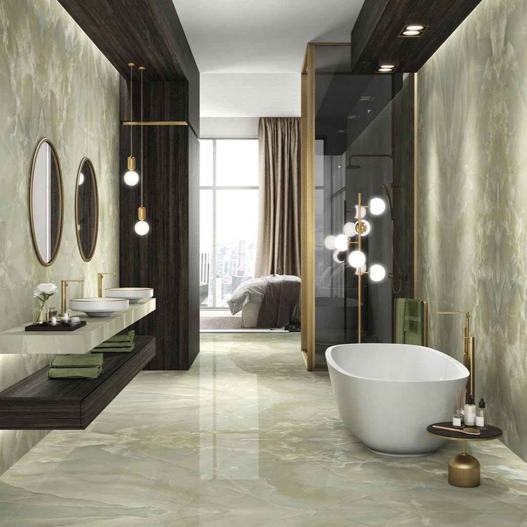 Badkamer met groene marmerlooktegels, een wit vrijstaand bad, donkere houttinten en goudkleurige accenten.