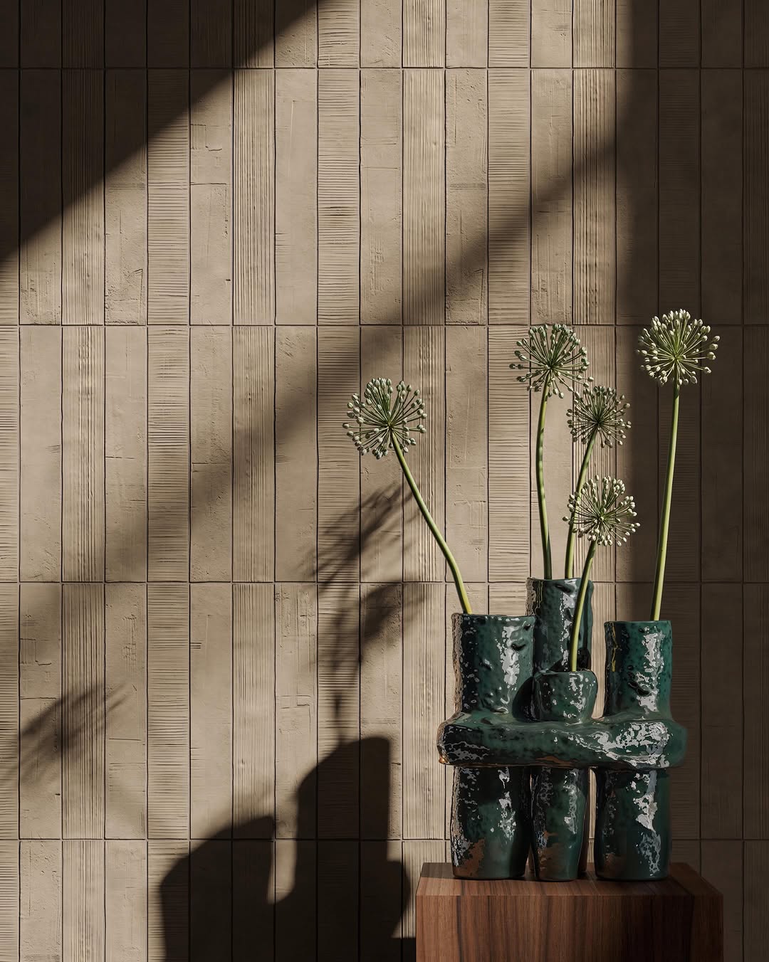Beige Kore-wandtegels met afwisselend reliëf, naast een donkergroene vaas met bloemstelen op een houten sokkel.