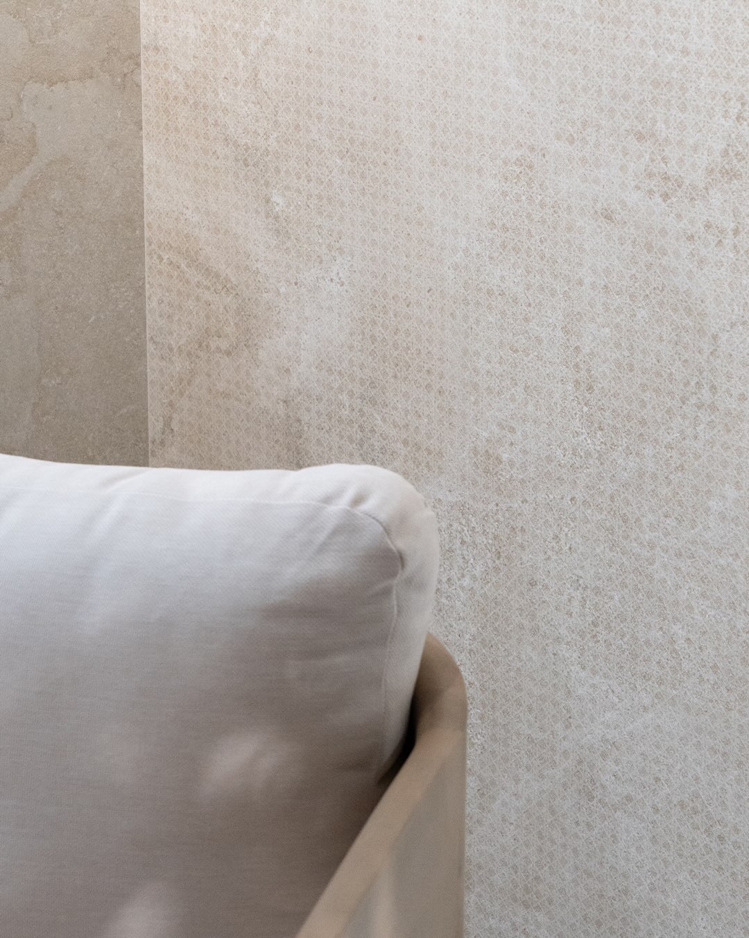 Lichte Portland-wand met fijne geometrische Weave-structuur achter een afgeronde stoel met wit kussen.