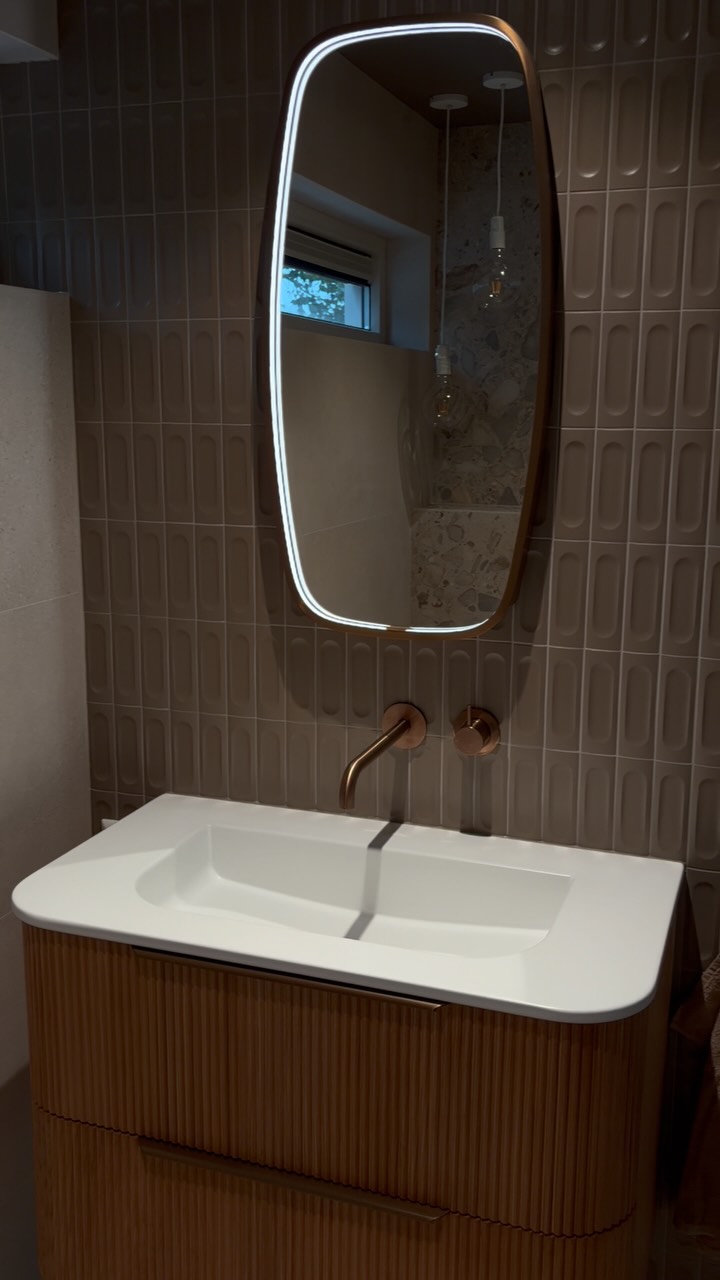 Reliëftegels achter een witte wastafel met koperkleurige wandkraan bij TONSCHOLTEN. Tegels & Sanitair in Uitgeest